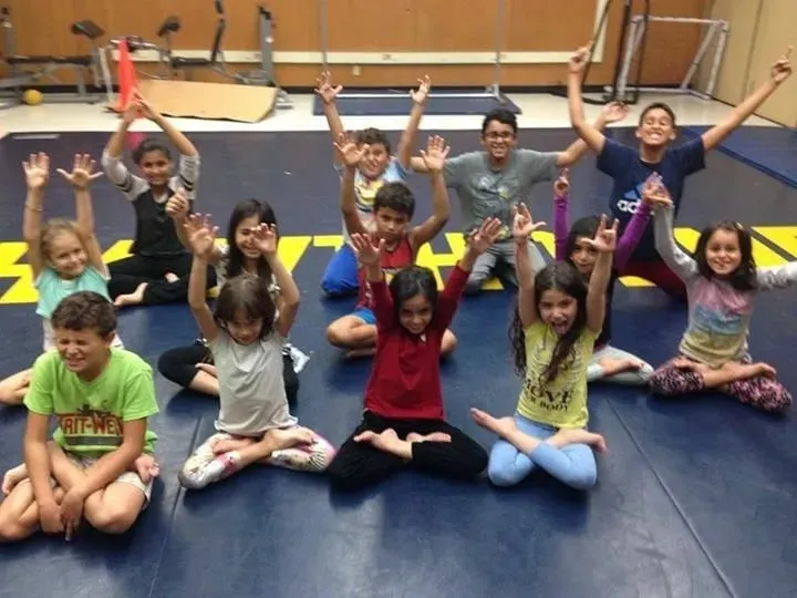 Children sitting on a mat with their arms raised high, smiling